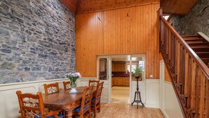 A dining area with a wooden table and chairs, a stone wall, and a wooden staircase.