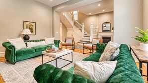 A spacious living room with a green velvet sofa set, a coffee table, and a staircase leading to an upper floor.