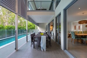 Un espace repas extérieur moderne, doté d’une piscine, de rampes en verre et d’une salle à manger offrant une vue panoramique.