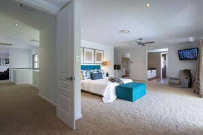 Une chambre à coucher avec un lit, un pouf bleu, une télévision et un ventilateur de plafond.