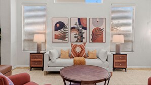Een woonkamer met een bank, twee bijzettafels, een ronde salontafel en drie kunstwerken aan de muur.