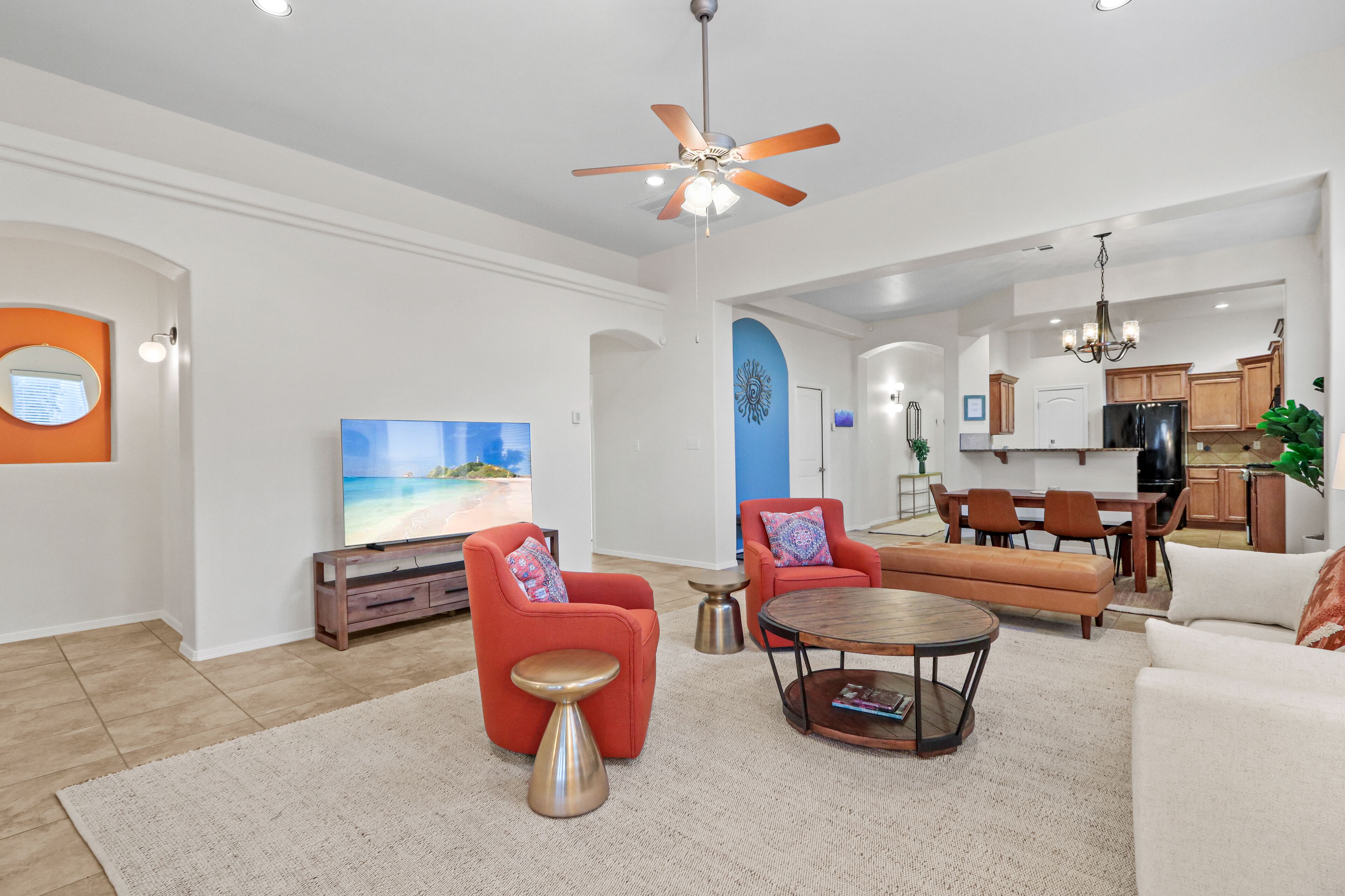 A spacious living room with a flat-screen TV, red armchairs, a coffee table, and a ceiling fan.