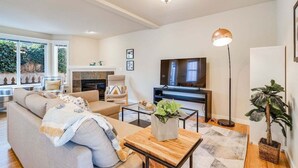 A modern living room with a sofa, coffee table, and a TV. There is a fireplace, a plant, and a floor lamp. - Perch - Walk to Lake Union! Spacious 3BR/3.5BA w/ Garage (Seattle)