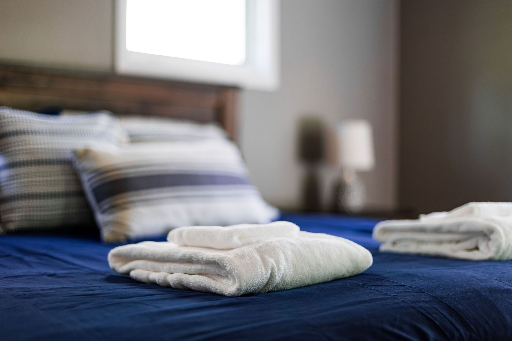 Una cama bien hecha con ropa de cama azul y toallas blancas dobladas al pie.