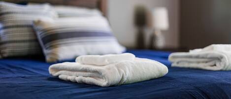 Una cama bien hecha con ropa de cama azul y toallas blancas dobladas al pie.
