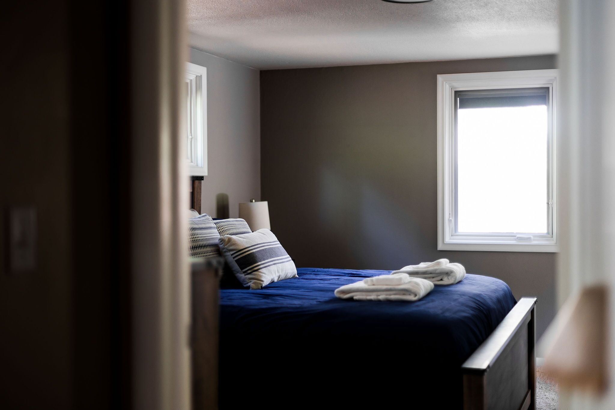 A bedroom with a bed, pillows, a window, and a view of the outside.