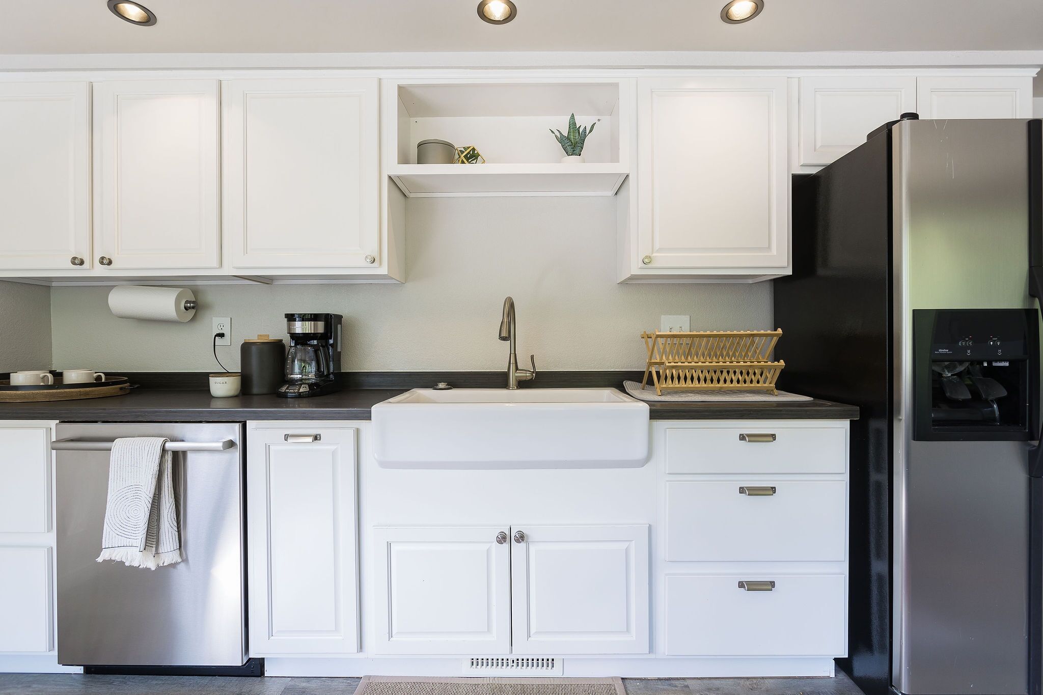 A modern kitchen with white cabinetry, a stainless steel refrigerator, and a built-in sink.
