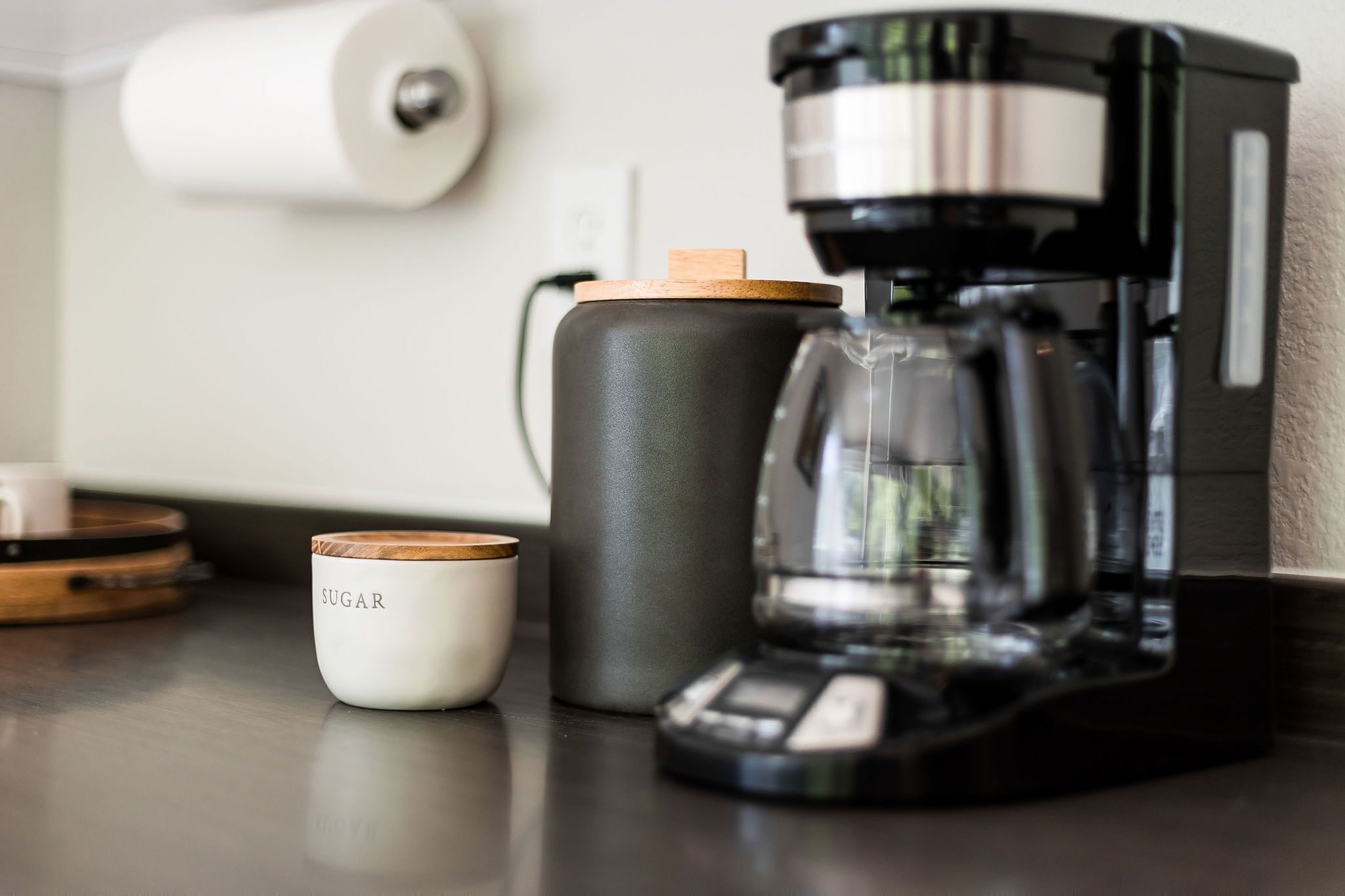 A coffee maker, a sugar container, and a roll of paper towels on a kitchen counter.