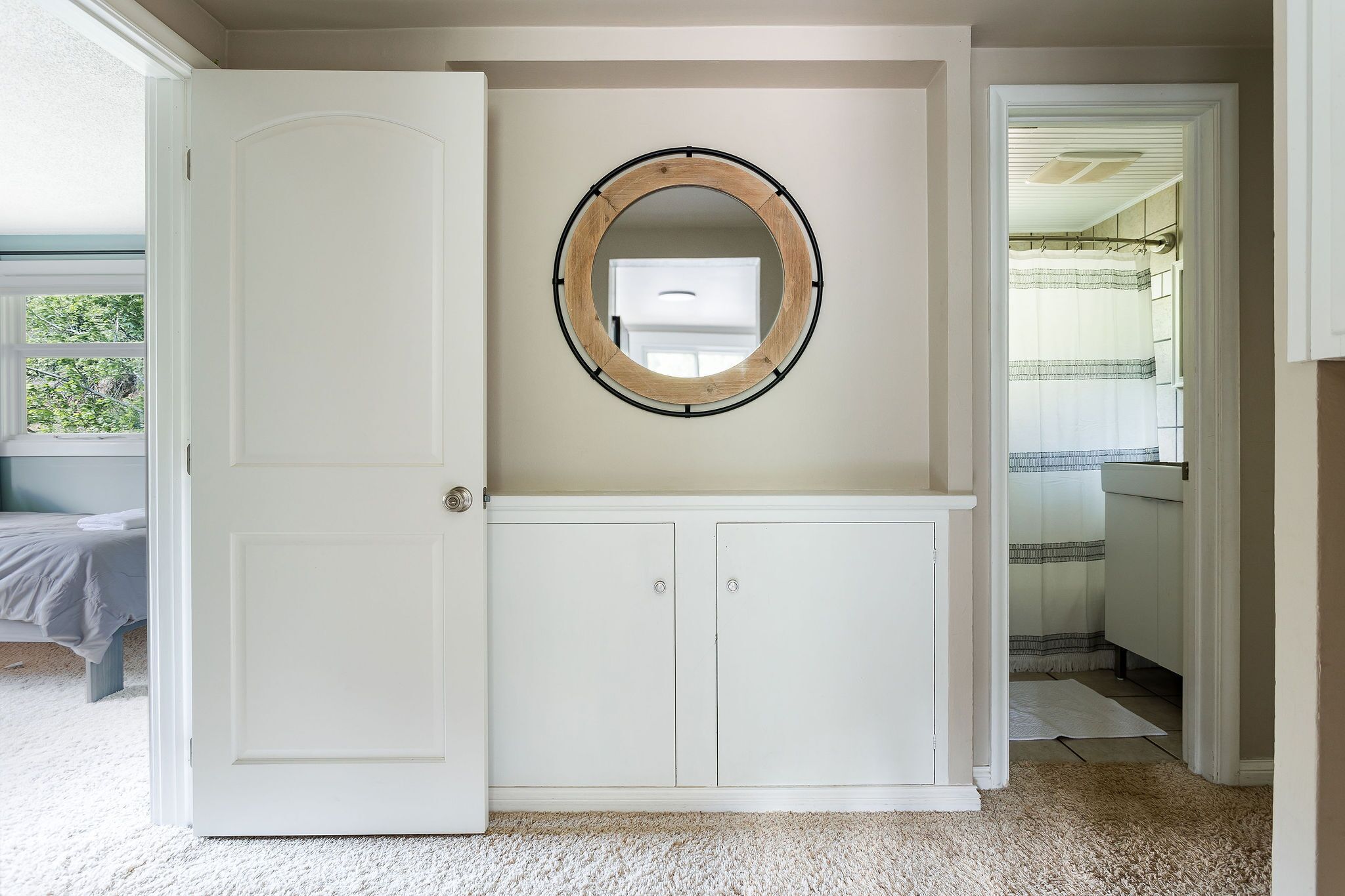 A room with a white door, a white cabinet, and a round mirror on the wall.