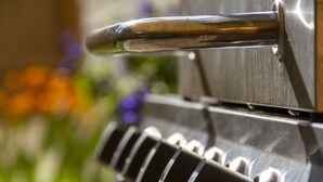 A close-up of a stainless steel barbecue grill with a handle and control knobs.