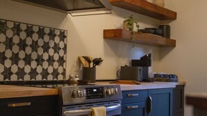 A kitchen with a stove, oven, and a backsplash with a geometric pattern. There are wooden shelves above the counter holding various kitchen items.