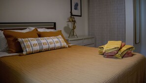 A neatly made bed with a patterned pillow, a brass lamp, and folded towels on a bedside table. - Brand New - Gracious Old Town Guest House w/ Hot Tub (Fort Collins)