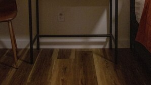 A room with a round mirror, a bedside table with a lamp, and a bed with a blanket.