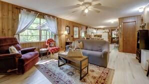 Una sala de estar acogedora con un sillón rojo, un sofá gris y un ventilador de techo de madera.