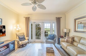 A living room with a sofa, a rocking chair, a patterned armchair, a coffee table, and a ceiling fan.