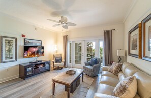 Ein Wohnzimmer mit Fernseher, Deckenventilator, Sofa, Sessel und Couchtisch.