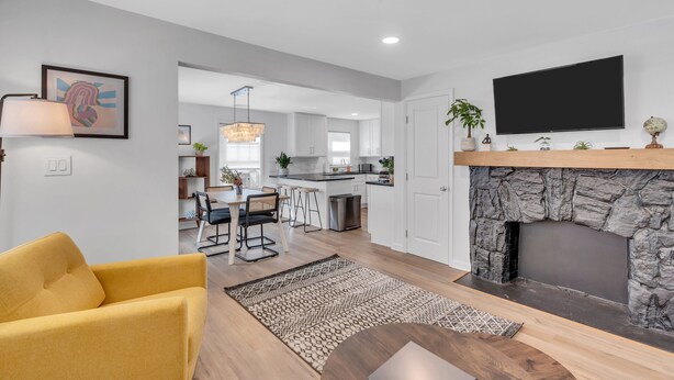 A modern living room with a fireplace, a dining area, and a kitchen in the background.