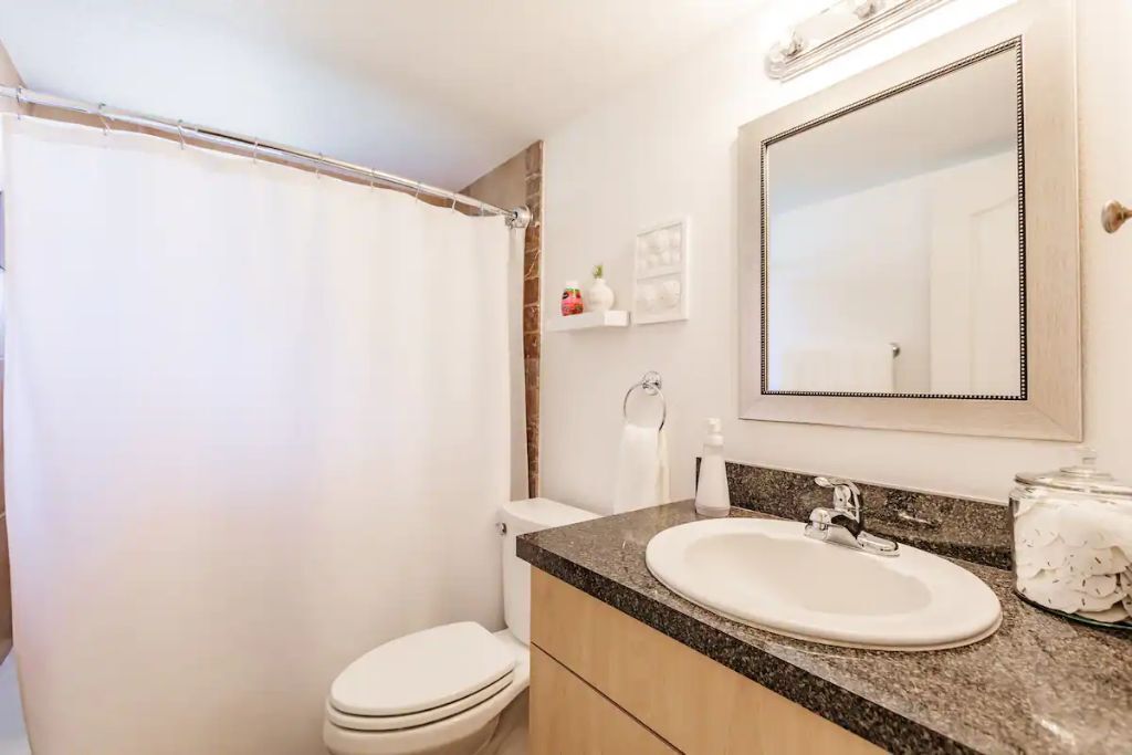 A bathroom with a shower curtain, toilet, sink, and mirror.