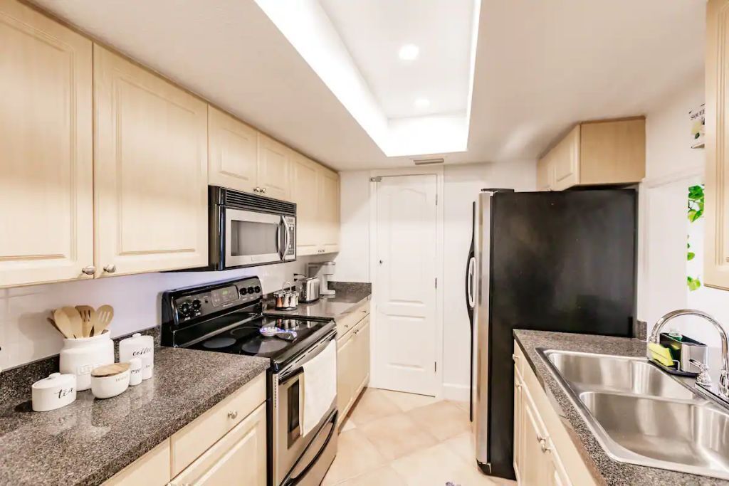 A modern kitchen with white cabinets, a black refrigerator, a microwave, a stove, and a sink.