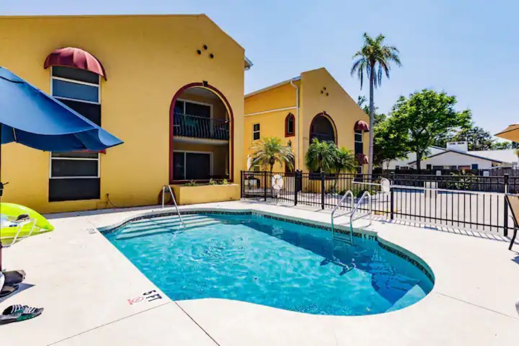 A swimming pool with a curved edge, surrounded by a yellow building with arched windows and balconies.
