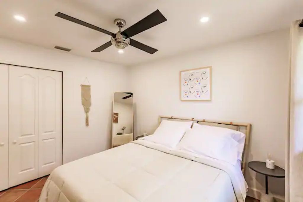Une chambre à coucher comprenant un lit, un ventilateur de plafond, une table de chevet et une œuvre d’art accrochée au mur.