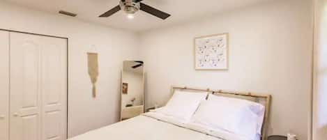 Une chambre à coucher comprenant un lit, un ventilateur de plafond, une table de chevet et une œuvre d’art accrochée au mur.