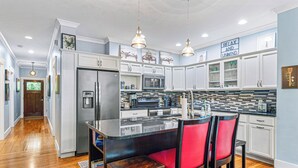 Una cocina moderna con armarios blancos, una isla central con sillas rojas, electrodomésticos de acero inoxidable e iluminación colgante.