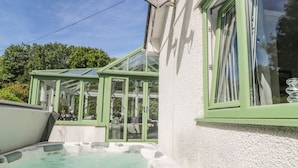 A hot tub and a glass-enclosed patio area adjacent to a building with a green window frame. - Cornerstone (Penzance)
