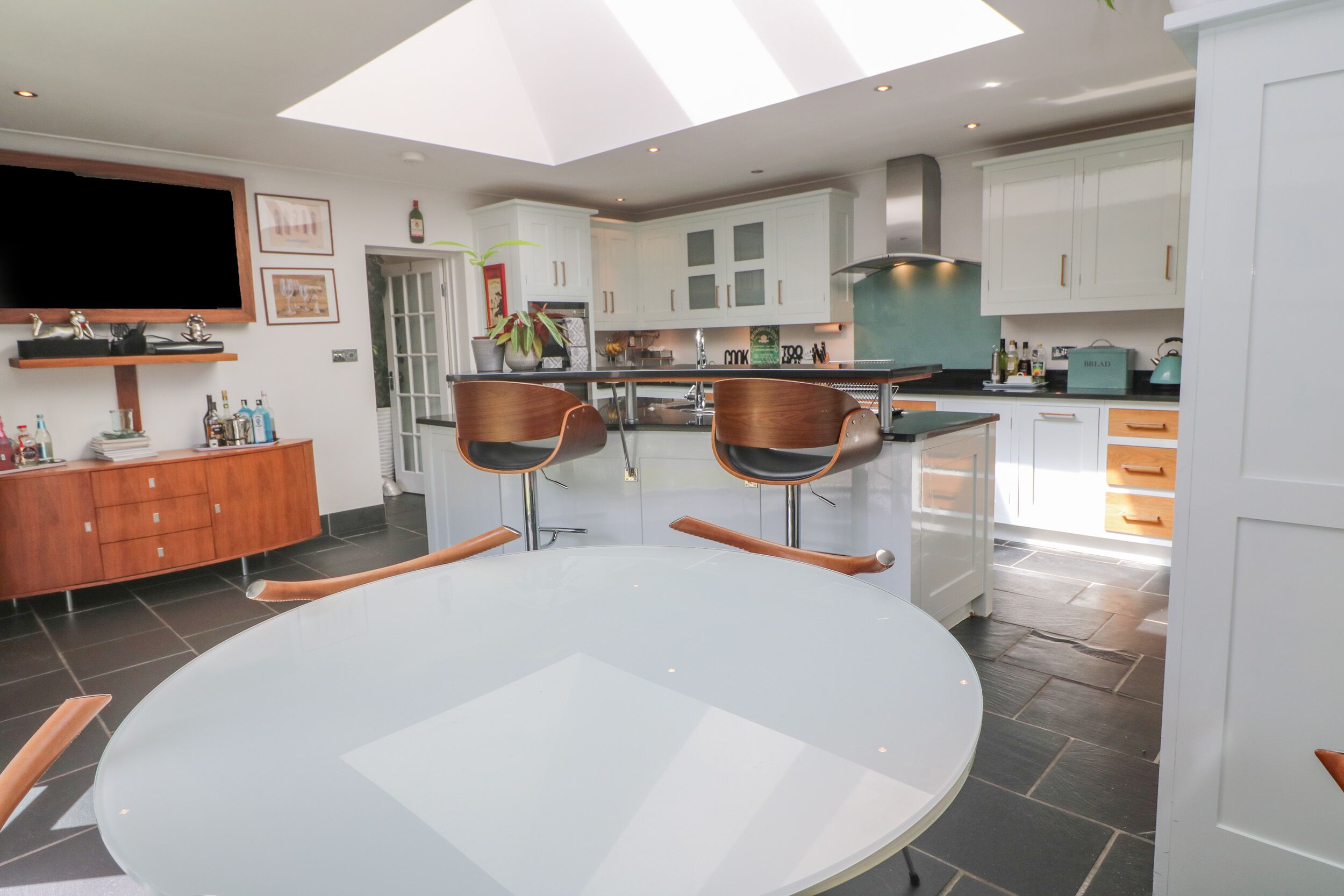 A modern kitchen with white cabinets, a dining table with two chairs, and a large window providing natural light.