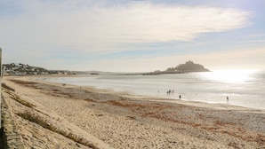 A beach with a sandy shore, a few people walking, and a distant hill. - Cornerstone (Penzance)