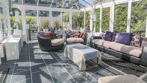 A conservatory with a glass ceiling, furnished with sofas and chairs, a table, and potted plants. - Cornerstone (Penzance)