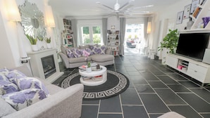 A modern living room with a fireplace, a round coffee table, and a large TV. - Cornerstone (Penzance)