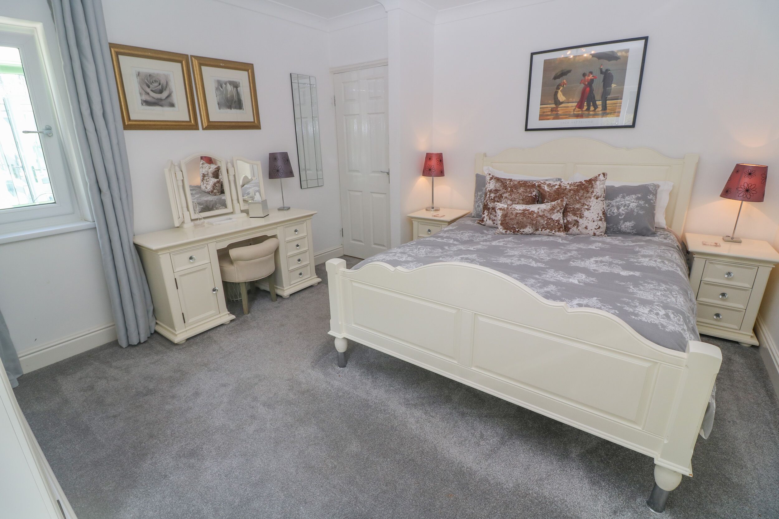 A bedroom with a bed, bedside tables, a dresser, and a desk.
