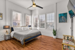 A bedroom with a bed, a ceiling fan, a nightstand, a lamp, a potted plant, and a chair. - Stunning 2BR | Balcony | Historic Luxury (New Orleans)