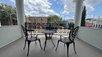 Een overdekt balkon met een tafel en stoelen, witte zuilen en uitzicht op gebouwen en bomen.