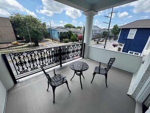 A balcony with a table and two chairs, a decorative railing, and a view of the neighborhood. - Stunning 2BR | Balcony | Historic Luxury (New Orleans)