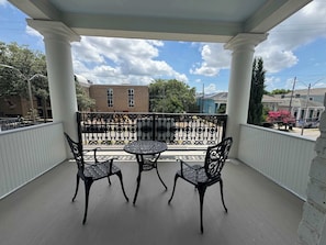 A covered balcony with a table and chairs, a view of buildings, and a clear sky.