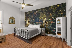 A bedroom with a bed, a ceiling fan, a nightstand, a cabinet, and a wall with a floral mural.