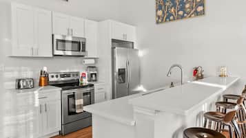 A modern kitchen with white cabinetry, stainless steel appliances, a central island with stools, and a decorative wall piece.