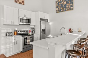 A modern kitchen with white cabinetry, stainless steel appliances, a central island with stools, and a decorative wall piece.