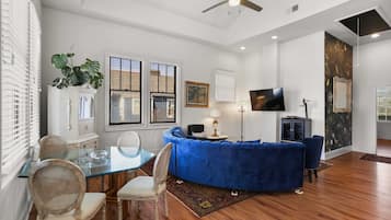 A modern living room with a glass dining table, blue sofa, and a flat-screen TV.