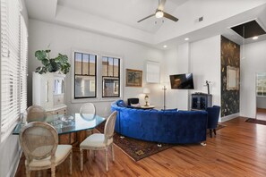 A modern living room with a glass dining table, blue sofa, and a flat-screen TV.