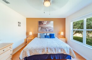 Relax in this serene bedroom with a large bed, bedside tables, and a window offering a view of lush greenery.