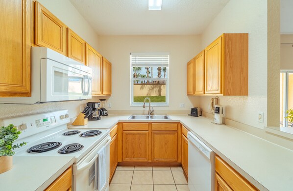 Kitchen with microwave and stove, sink, and window offering a view of palm trees and a house.