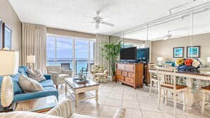 Een ruime woonkamer met een grote televisie, comfortabele zithoek, een eethoek en een balkon met uitzicht op de oceaan.