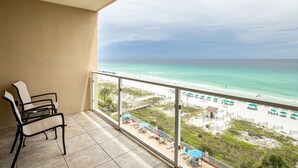 Een balkon met uitzicht op het strand, stoelen en parasols.