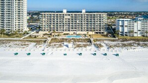 Een strandhotel met meerdere gebouwen, een zwembad en een zandstrand met parasols.