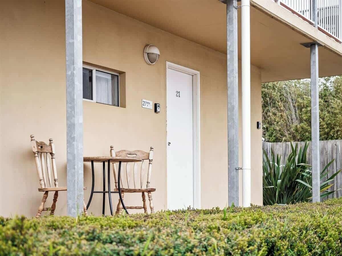 A building with a beige exterior, a door marked with the number 21, a small window, and a table with two chairs outside.