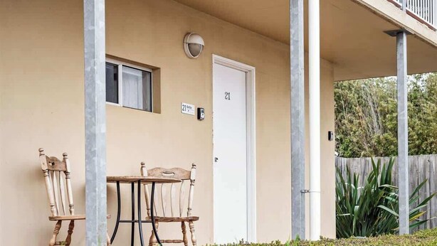 A building with a beige exterior, a door marked with the number 21, a small window, and a table with two chairs outside.