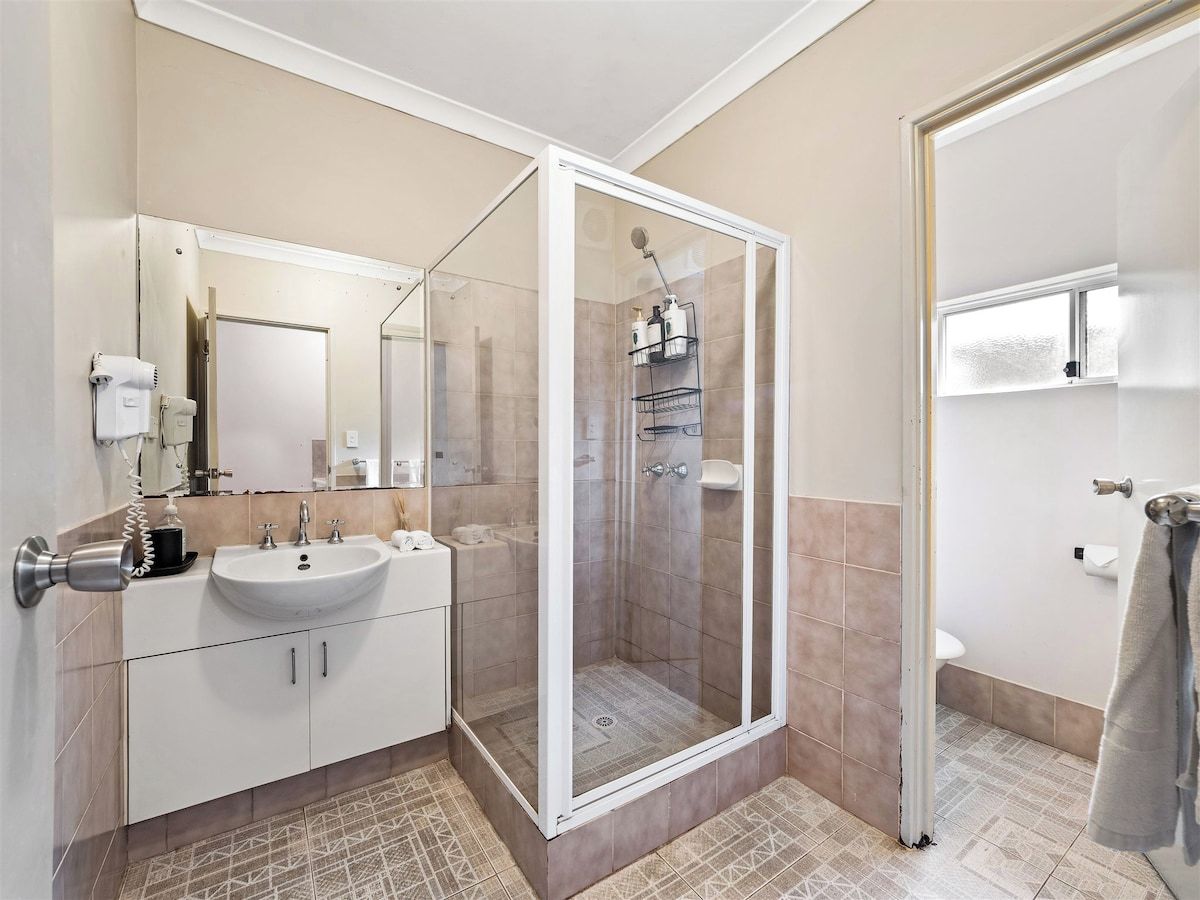 A bathroom with a glass-enclosed shower, a sink with a mirror, and a toilet.